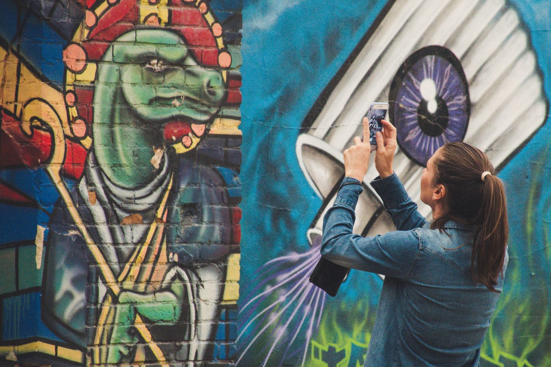 Kobieta fotografuje kolorowy mural graffiti na ścianie w mieście