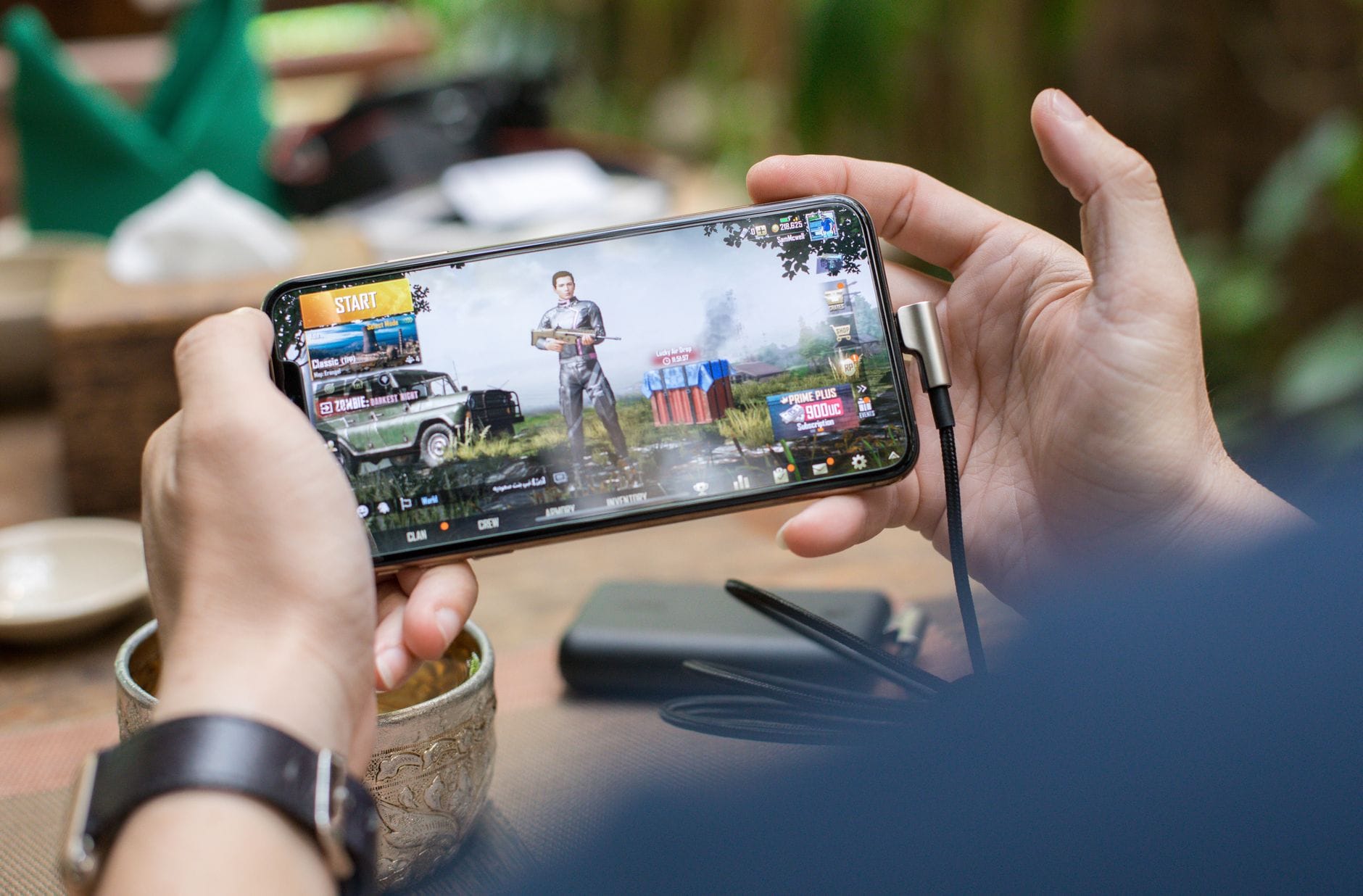Osoba grająca w PUBG Mobile na smartfonie na dworze, telefon podłączony do ładow