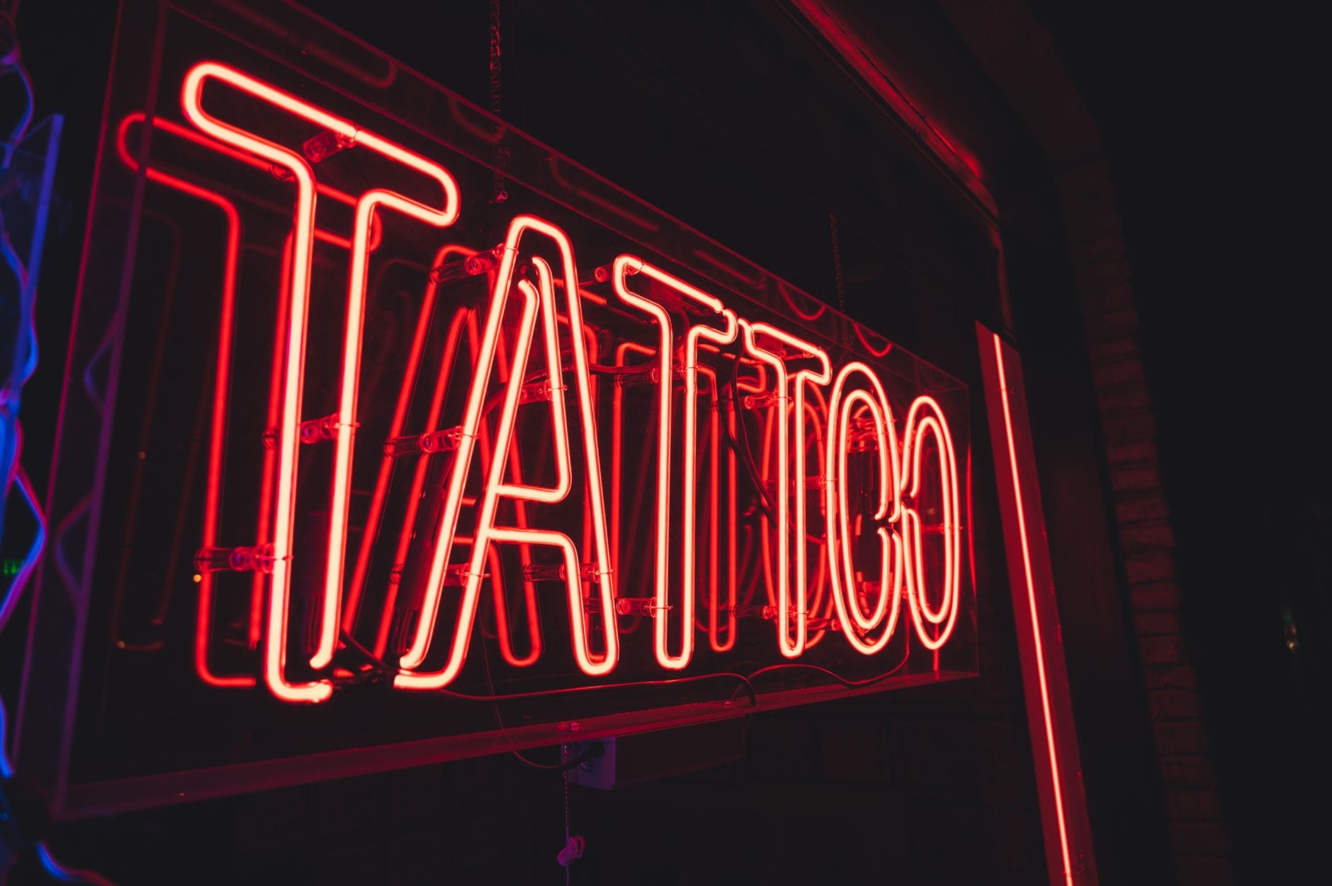 Zbliżenie na świecący neonowy szyld tattoo w miejskim otoczeniu